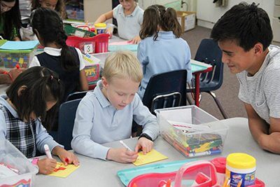 Upper school student helping first grade student make a poster