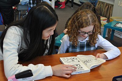 Upper school student and fourth grader reading together at the reading assembly