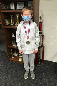 Josh Murr in front of math trophy case wearing medal
