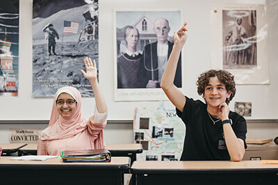 Two high schools students raising hands in social studies