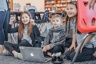 Three Lower School students are working on a laptop. 
