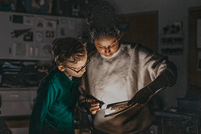 Ms. Kimmerle and a student look at a book with a flashlight.