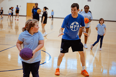 A MPA P.E. teacher and Lower School student playing basketball. 