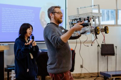 Instructor with small robot and upper school student giving a speech