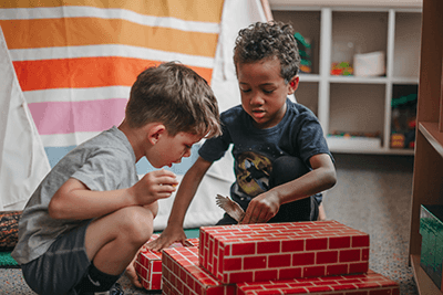 Two PreK students are building with brick blocks together